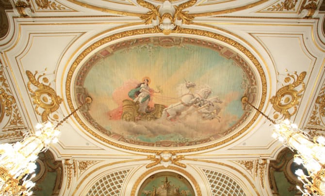 Una fotografía de la pintura en el techo de la sala Asahi no Ma. La imagen de la deidad romana del amanecer, Aurora, con el sol naciente a sus espaldas, y conduciendo galantemente un carruaje tirado por caballos blancos por una brecha entre las nubes.