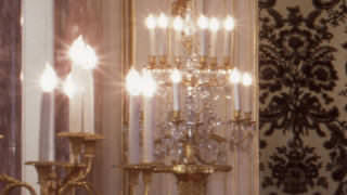 Una fotografía de un candelabro de grandes dimensiones en la sala Asahi no Ma. Una bombillas en forma de llamas de fuego iluminan con resplandor el candelabro dorado.