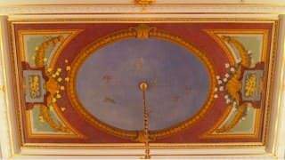 A photo of the ceiling painting in the great hall. It is laid out to appear as though one is looking up at part of a building, where the center portion represents the expansive sky, where seven doves are painted.