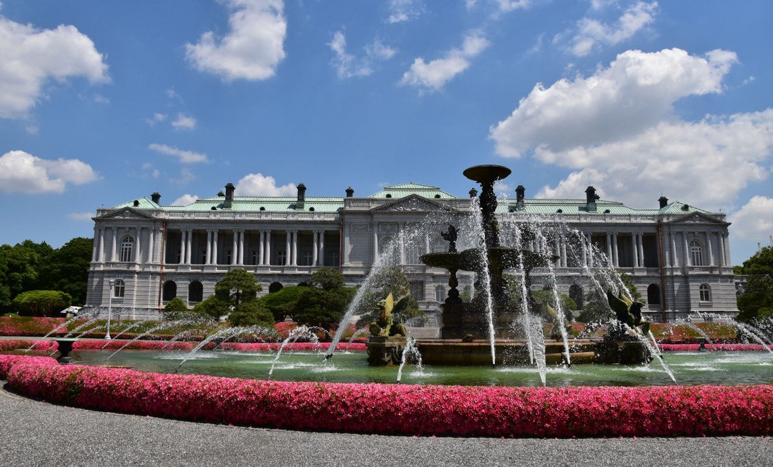 Una fotografía de la fuente de delante de la Casa de Invitados del Estado, Palacio de Akasaka, rodeada de flores de intenso color rosa.