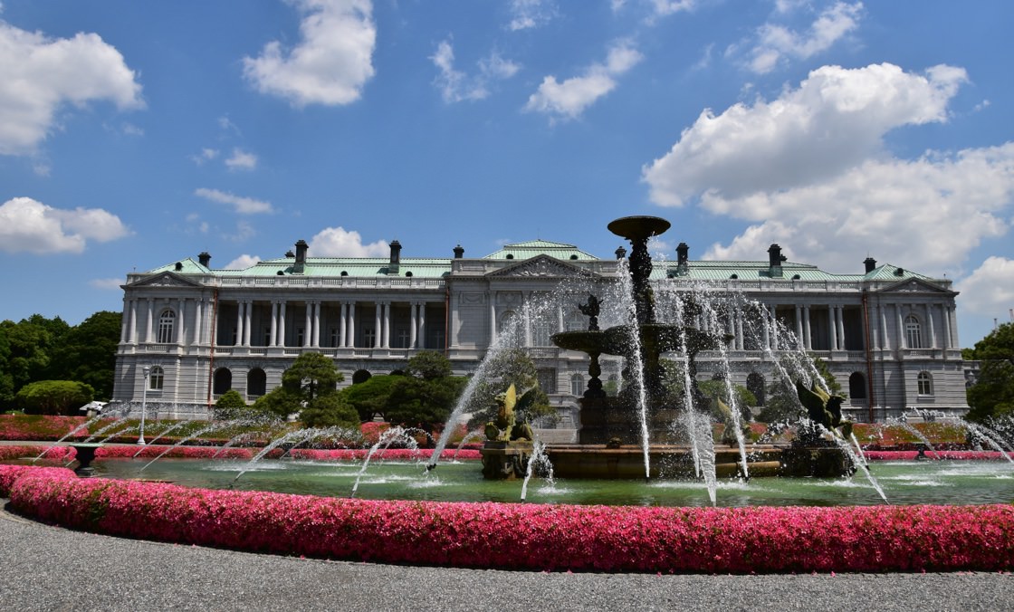 鮮やかなピンク色の花に囲まれた迎賓館赤坂離前の噴水の写真。