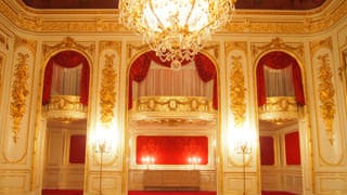 Una fotografía del foso de orquesta de la sala Hagoromo no Ma. El foso de orquesta está construido en una segunda planta de la habitación. Sus cortinas ornamentales rojas y sus relieves de estuco bañado en oro son característicos.