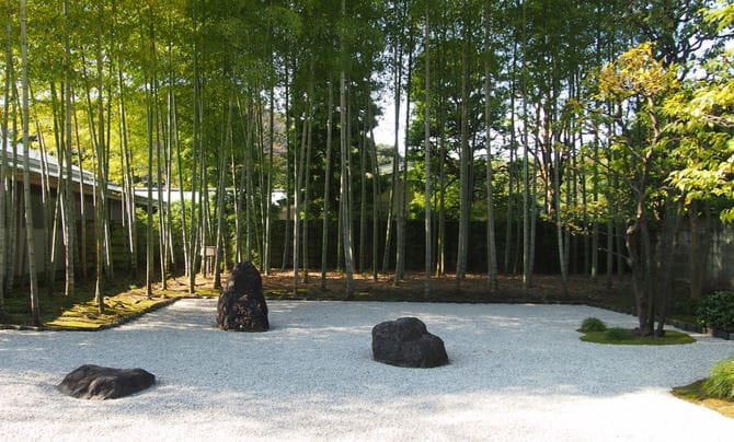 Una fotografía del jardín interior del anexo japonés. El suelo está cubierto de gravilla de color blanco y en el centro tiene colocadas tres piedras traídas desde Kifune, al norte de la ciudad de Kioto. El bambú Moso crece detrás de las rocas.