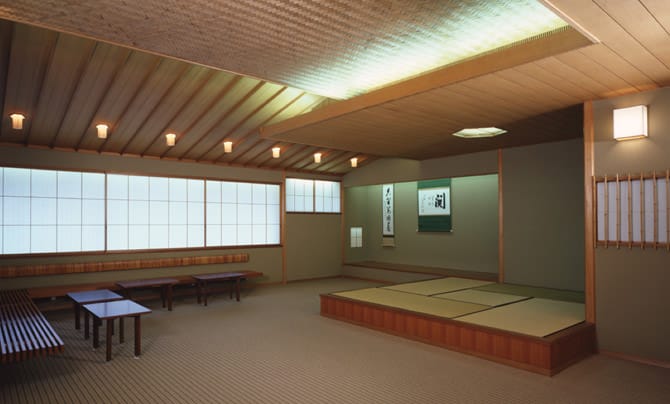 Una fotografía de la sala de té del anexo japonés Se han colocado numerosos asientos al lado de la pared, además de un espacio de tatami que mide cuatro esteras y media. Se expone un rollo colgado en la alcoba Toko no Ma en el fondo de la sala. 