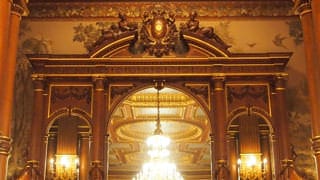 A photo of the sideboard in Kacho no Ma. There is a large mirror atop the carved wooden sideboard, and towards the top, the Imperial chrysanthemum emblem can be seen.