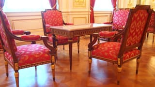 Une photo des chaises et des tables de la salle Sairan no Ma. Un motif est brodé sur la partie en tissu rouge des chaises.