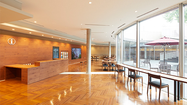 A photo of the rest area in the lower level. Natural light comes through the glass from the central courtyard, and the inside of the building is brightly lit, with chairs facing the window to the right, and an information desk to the left.