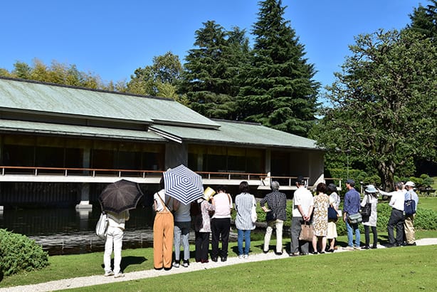 和風別館庭園的參觀景況,參觀者並排於和風別館前的池塘旁,聽著導覽員的解說。