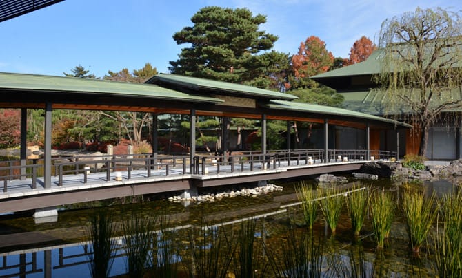 Against a background of the garden, in which the trees have slightly begun to change colors, the bridge appears broad stretching over the pond, connecting the eastern and western eaves. Nebikigusa (sedge, a type of rush) grows in the pond in the foreground.