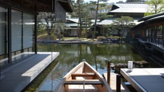 Une photo du bateau « wasen » à son quai. Au premier plan, on aperçoit le bateau en bois et, au loin, l'étang et l'avant-toit de l’est de la Maison des hôtes d'État de Kyoto.