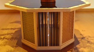 A photo of the pedestal beneath the flower vase. The pedestal is octagonal. The table foot also has eight sides. The side facing front is made of strips of lacquered wood and mother-of-pearl, evenly lined up. The faces of the pedestal base on either side are decorated with woven patterns of finely sliced bamboo.