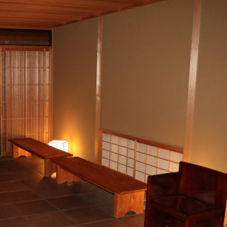 A photo of a smooth, earthen wall illuminated by a floor lamp. Two benches are placed in front of the wall.