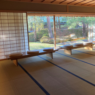 A photo of a room with large tatami mats, facing a large window looking out on a garden. 