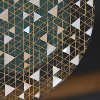 A photo of a geometric pattern of mother-of-pearl inlaid in the shape of many triangles within a larger circle onto a black surface.