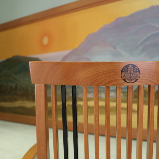 A photo of the wooden back of a chair, carved with the emblem of the State Guest House. Behind the chair hangs a tapestry of the mountains of Kyoto.