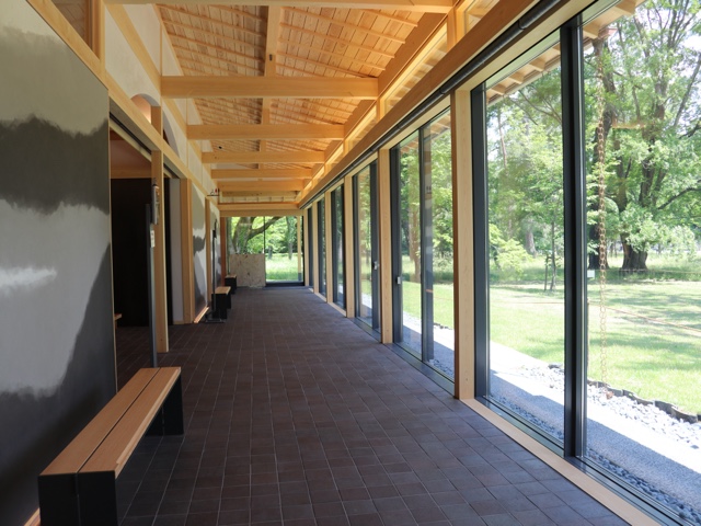A photo of a hallway with benches, facing a wall of glass panels looking out a grassy lawn with trees.