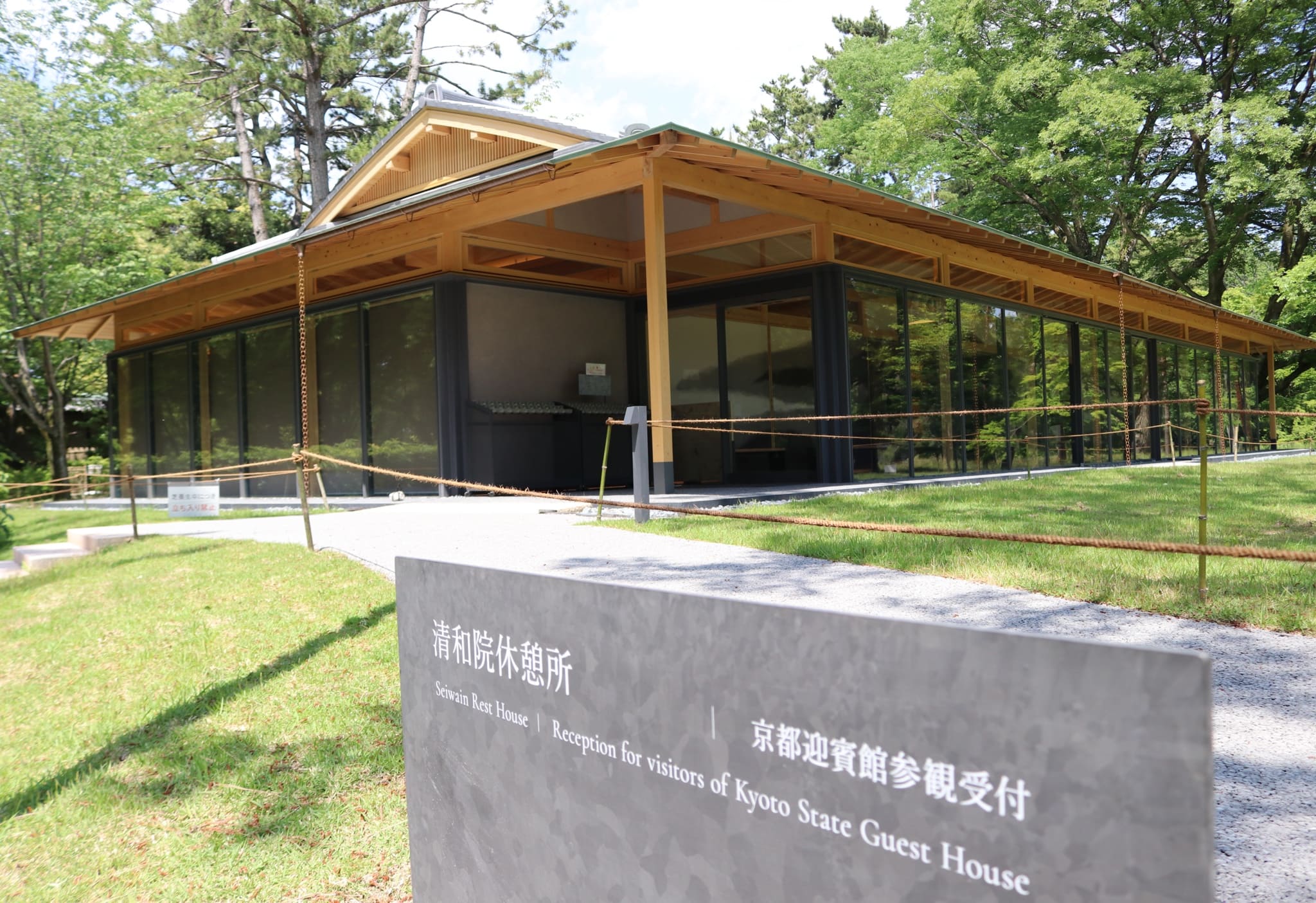 A photo of the exterior of the Sewain Rest House, with a placard in front. The modern building has glass walls and a roof with elements of traditional Japanese architecture.