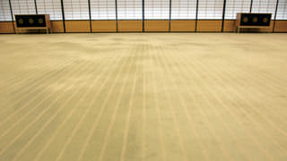 A close-up photo of the carpet in Yubae no Ma. There are white stripes in the carpet. If you look closely at these stripes, you can see bead-like shapes made to suggest the pebbles of a pond. Further examination of the pattern in the carpet reveals the shapes of white clouds floating in a pond.