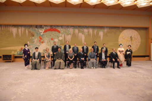The delegation is seated side-by-side in two rows in front of the Tuzure-ori tapestry Reika in Fuji no Ma room for a commemoration photo.